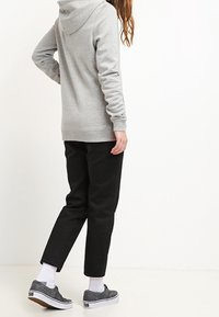 Sudadera gris con capucha, pantalones negros ajustados, calcetines blancos y zapatillas grises. Enfoque en un ajuste relajado y estilo casual.