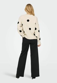 Pull crème avec de grands pois noirs, coupe décontractée, poignets et ourlet côtelés. Associé à un pantalon noir à jambes larges et des talons hauts.