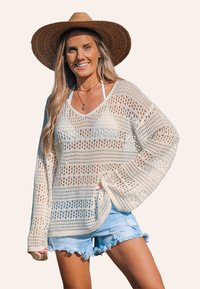 Pull en crochet léger, crème, avec un tissage ouvert, des manches longues et une coupe décontractée. Associé à un short en denim effiloché.