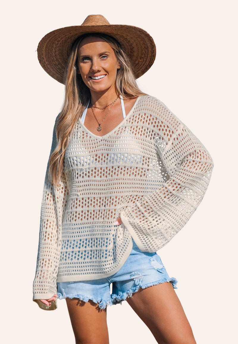 Pull en crochet léger, crème, avec un tissage ouvert, des manches longues et une coupe décontractée. Associé à un short en denim effiloché.