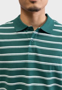 Green striped polo shirt featuring white horizontal stripes, a buttoned collar, and short sleeves made of soft cotton material.