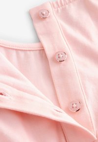 Heller pinker Stoff mit glatter Textur, ausgestattet mit roségoldenen Knöpfen und einer Knopfleiste. Weicher Kragen und sichtbare Nähdetails.