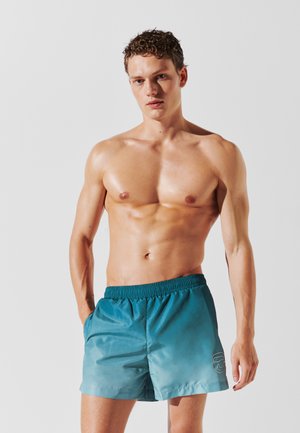 Shorts da bagno turchesi realizzati in tessuto morbido, con un design a gradiente, cintura elastica e un logo discreto sul lato sinistro inferiore.