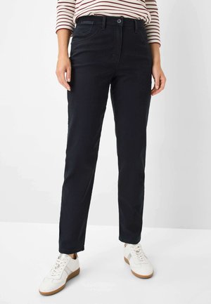 Dunkelblaue Jeans im klassischen Schnitt, fünf Taschen und einem vorderen Knopfverschluss, kombiniert mit weißen Sneakers für einen Kontrast.