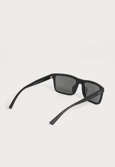 Lunettes de soleil rectangulaires noires, avec des verres gris foncé et des branches fines, présentées sur un fond clair. Le logo A|X figure sur une branche.