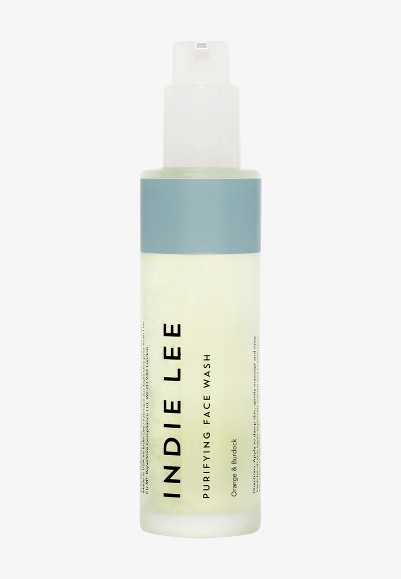 Bouteille transparente de nettoyant pour le visage purifiant INDIE LEE, avec un capuchon bleu clair, arborant un texte noir en gras, et un liquide jaunâtre à l'intérieur.