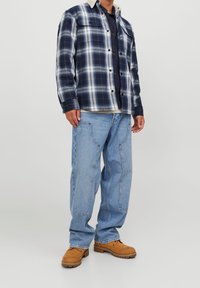 Rutig skjorta i marinblått och vitt med knappad krage och metalltryckknappar. Buren med ljusblå jeans och bruna arbetskängor.