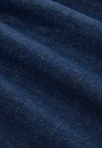 Primer plano de tela de mezclilla azul oscuro que muestra detalles de textura y tejido con pliegues sutiles y reflejos.