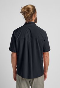 Zwarte shirt met korte mouwen, ontspannen pasvorm, lichte stof en een rugnaad; gedragen met lichtgekleurde broek.