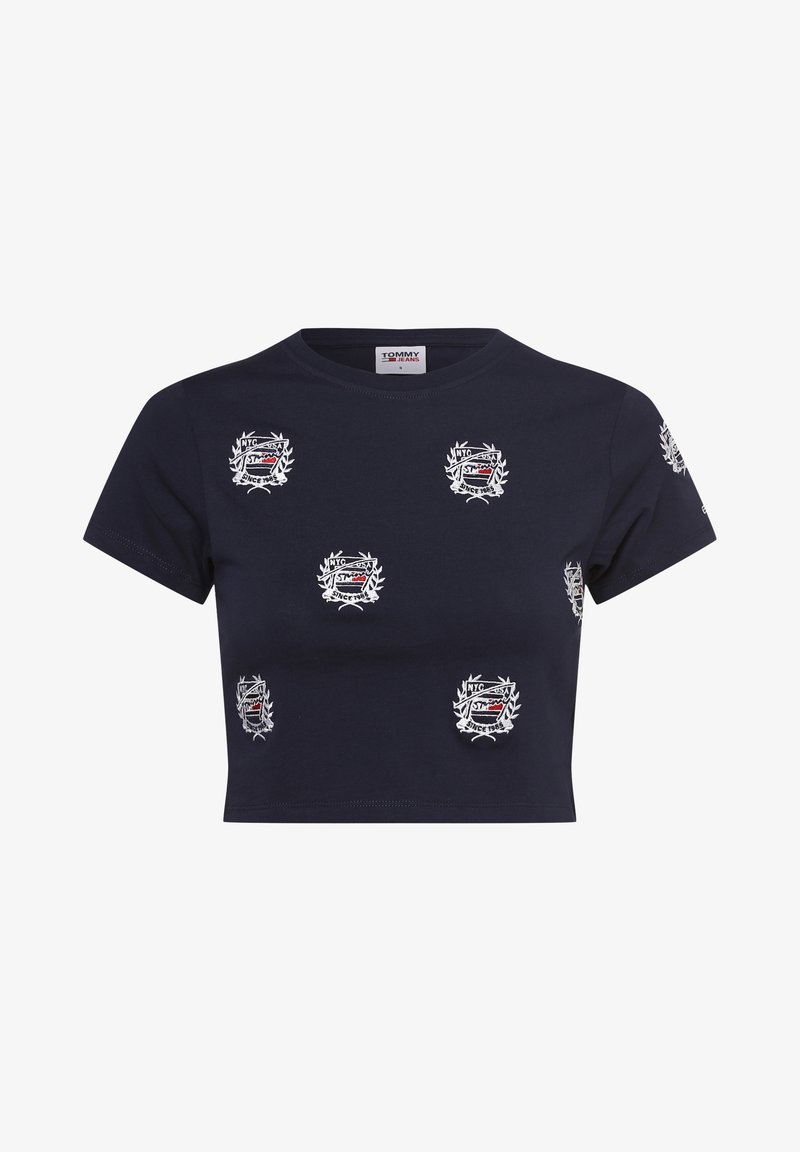 T-paita, joka on tummansininen ja lyhytmallinen, valmistettu puuvillasta sekä pyöreällä kaula-aukolla. Sisältää useita valkoisia ja punaisia brodeerattuja embleemejä, joiden ympärillä on laakeriseppeleitä.