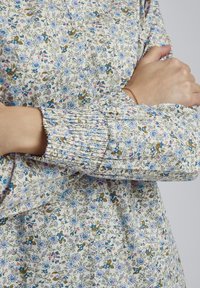 Blütenmusterstoff in Creme mit blauen, pinken und grünen Blumen. Geraffte Bündchen mit lockerer Passform und geraffter Textur.