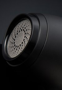 Gros plan sur un rasoir à tissu noir avec une tête en maille métallique circulaire comportant des perforations et le logo "ghd" au centre.