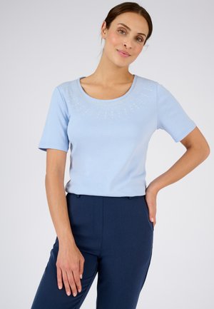 Top azzurro chiaro a maniche corte con scollo rotondo decorato con borchie argentate, abbinato a pantaloni su misura blu scuro.
