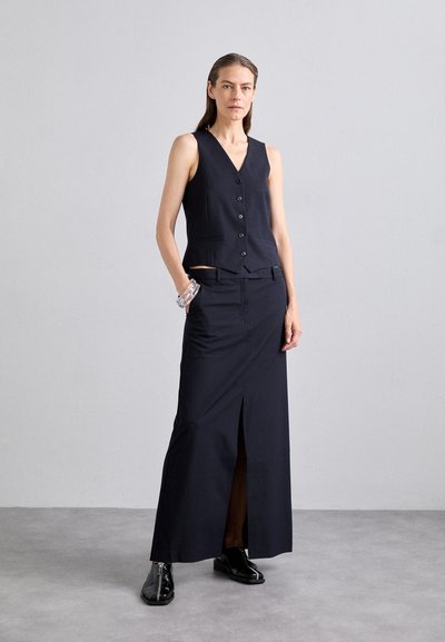 Navy vest and maxi skirt set made from smooth fabric, featuring a V-neck, six buttons, side slit, and sleek, glossy black shoes.