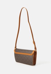 Brun mönstrad väska med lång beige rem. Texturerat material med geometriskt mönster, rundad form och lockstängning.