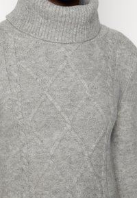 Maglione grigio a collo alto lavorato a maglia, realizzato in materiale morbido, con un motivo a rombi e collo a costine. La texture appare confortevole e calda.