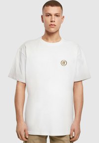 Hvid bomulds-t-shirt med rund halskrave og korte ærmer. Har et lille broderet logo i guld på venstre brystområde.