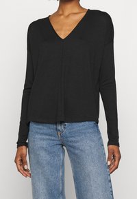 Haut noir à manches longues avec un design à col en V, présentant une coupe décontractée et une texture douce, associé à un jean large bleu clair.