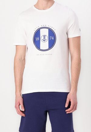 Weißes Baumwoll-T-Shirt mit einem blauen, runden Logo, das "Lyle and Scott", "1874" und ein Distel-Design zeigt; kurze Ärmel und Rundhalsausschnitt.
