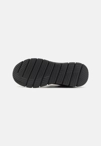 Semelle de basket en caoutchouc noir avec un motif de semelle, présentant des nervures horizontales et des sections surélevées pour l'adhérence et la traction.