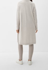 Ljusgrå lång cardigan med ribbade mudd, i kombination med beiga leggings och vita sneakers. Slät, mjuk textur med avslappnad passform.