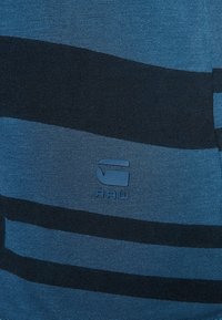 Blårandig tygtröja med mörkblå horisontella ränder, slät textur och en liten "RAW"-logotyp tryckt på bröstet.