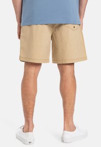 Shorts din bumbac bej, cu croială dreaptă, față plată și buzunar posterior vizibil. Asortați cu adidași albi și o cămașă albastră.