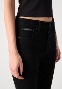 Černé džíny z denimu mají klasický design s viditelnou štítkovou logem Calvin Klein blízko kapsy. Materiál má hladkou strukturu a těsně přiléhá.