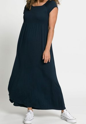 Marineblå maxi kjole med firkantet halsudskæring, korte ærmer og smocked liv. Det flydende stof skaber en afslappet silhuet. Bæres med hvide sneakers.
