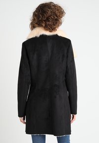 Cappotto in morbido suede sintetico nero con colletto in pelliccia sintetica beige. Vestibilità sagomata, design di lunghezza media, caratterizzato da cuciture verticali e maniche lunghe.