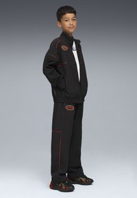 Czarna sportowa kurtka i spodnie z czerwonymi akcentami, z wyszywanym logo. Teksturowana tkanina została połączona z czarno-czerwonymi trampkami.