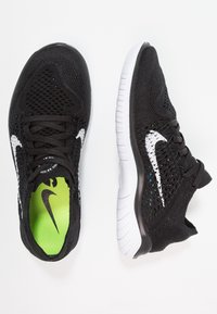 Zwarte sportschoenen met een ademend mesh bovenwerk, wit swoosh-logo en felgroene binnenzool, met een gestructureerde rubberen zool.