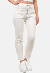 Pantalon blanc avec une taille à cordon, fermeture à cinq boutons à l'avant, et deux poches latérales. Complété par des baskets blanches.