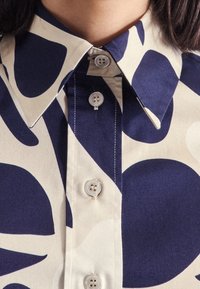 Collared blouse featuring a cream background with navy abstract patterns, button closure, and a smooth fabric texture.