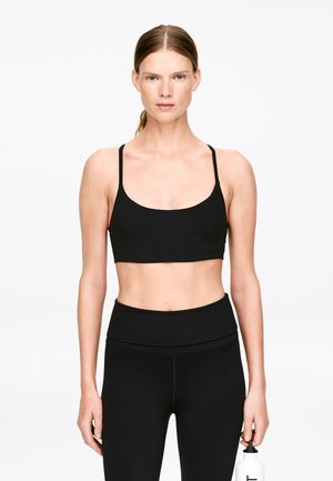 Schwarzes, sportliches Crop-Top mit dünnen Trägern und rundem Ausschnitt, kombiniert mit schwarzen Leggings mit hoher Taille. Glatte Textur und minimalistisches Design.