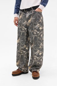 Lossen grijze broek met een bladeren- en takkenpatroon, gemaakt van denim. Gecombineerd met bruine instappers, wat een casual outfit laat zien.