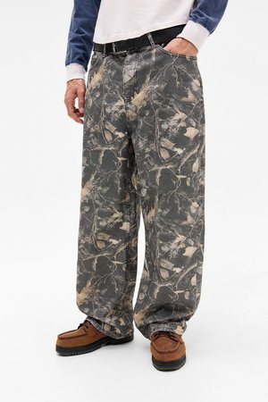 Baggy gray pants with leaf and branch pattern, made of denim. Paired with brown loafers, showcasing a casual outfit.