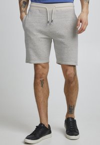 Shorts en jersey gris avec une taille élastique et un cordon de serrage. Présente des poches latérales et une coupe décontractée. Portés avec des baskets noires.