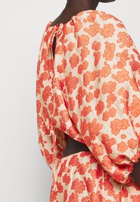 Kreemja ja punase lillemustriga pluus, millel on avar lõige, kokku volditud kaelus ja taga sidumisdetail. Valmistatud kergest kangast.