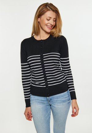 Schwarze Strickjacke mit weißen horizontalen Streifen, mit Rundhalsausschnitt, Knopfverschluss und gerippten Bündchen, kombiniert mit hellblauen Jeans.