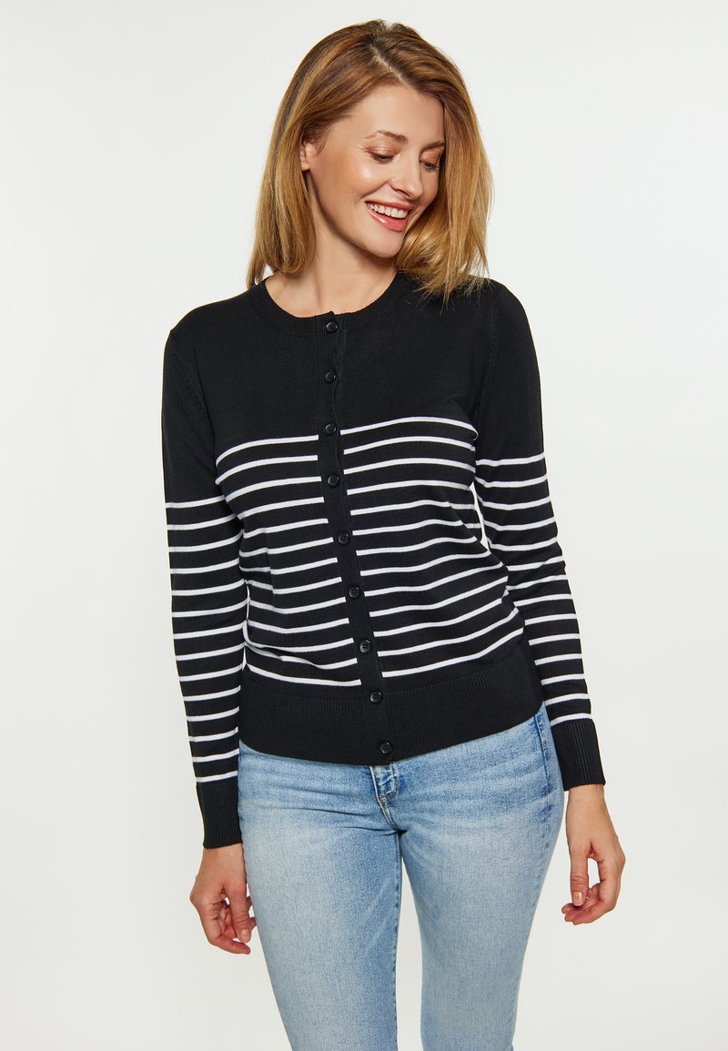 Cardigan nero con strisce orizzontali bianche, presenta un collo rotondo, chiusura con bottoni e polsini a costine, abbinato a jeans blu chiaro.