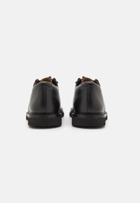 Chaussures en cuir noir avec une finition texturée, bout rond et semelle en caoutchouc noir. Lacets marron et détails de couture sur le dessus.