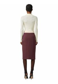 Top a maniche lunghe a coste color crema con un design aderente, abbinato a una gonna color borgogna di lunghezza al ginocchio. La modella indossa scarpe con tacco nere e collant.