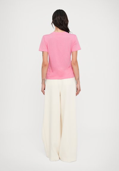 Ροζ κοντομάνικη μπλούζα με στρογγυλή λαιμόκοψη, συνδυασμένη με φαρδιά εκρού παντελόνια. Το ύφασμα φαίνεται απαλό με λείο υφή.