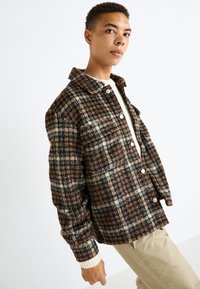 Braun karierter Blazer mit großen Knöpfen, strukturiertem Stoff und Kragen. Verfügt über cremefarbene Akzente an den Manschetten und Taschen.