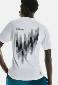 T-shirt en coton blanc avec un design graphique noir de lignes verticales et de points au dos, avec le texte "INGÉNIERIE SUISSE" au-dessus.