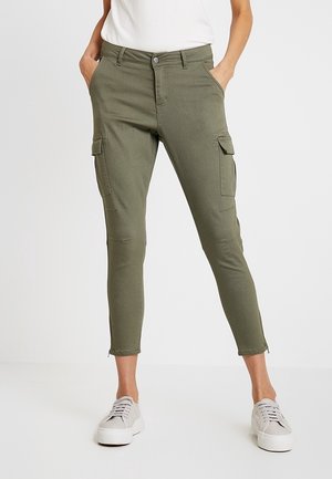 Pantalon cargo slim fit vert olive avec poches latérales, longueur raccourcie, porté avec des baskets blanches et un haut blanc.