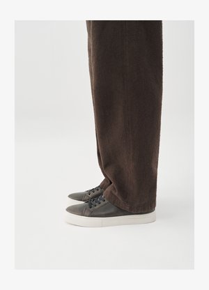 Dunkelbraune, strukturierte Hose kombiniert mit grauen Sneakern, die ein glattes Lederobermaterial, eine abgerundete Spitze und eine weiße Gummisohle aufweisen.