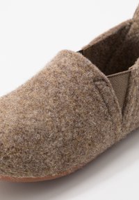 Chaussure brune en feutre à enfiler avec surface texturée et panneaux latéraux élastiques, dotée d'un bout rond et d'un design minimaliste. Matériau doux et flexible.