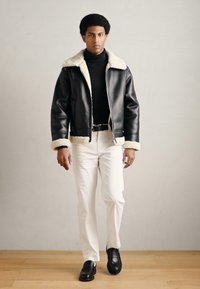 Czarna skórzana kurtka z kołnierzem z baranka, dopasowany czarny golf, białe spodnie i czarne loafersy. Prosty, nowoczesny design z kontrastującymi fakturami.